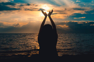 silhouette photo of a woman holding her hands up in the air near an ocean